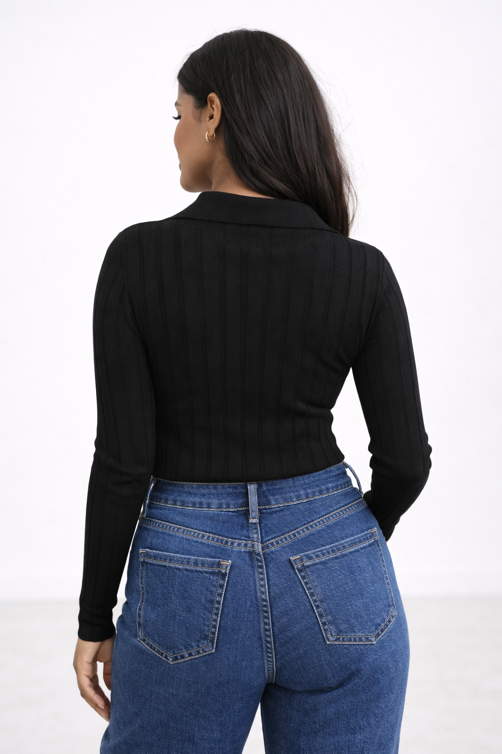 Person wearing a black long-sleeve top and blue jeans on a white background