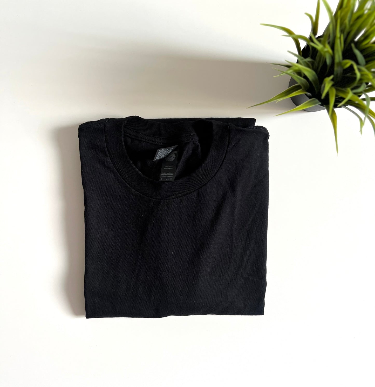 Folded black t-shirt on a white surface with a plant in the corner