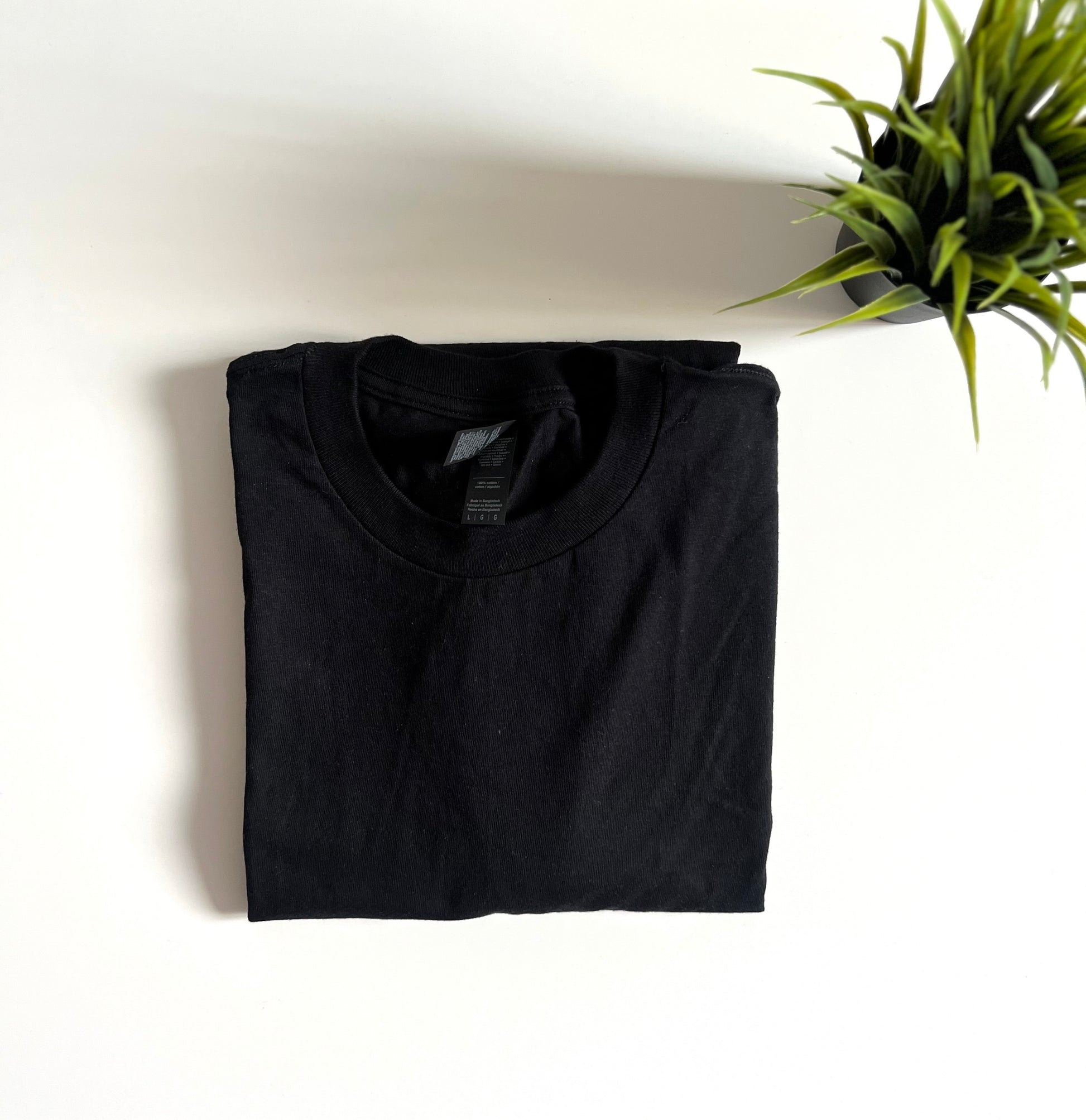 Folded black t-shirt on a white surface with a plant in the corner