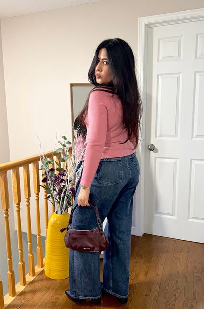Woman in pink sweater and blue jeans standing in a room with a yellow vase and plant.