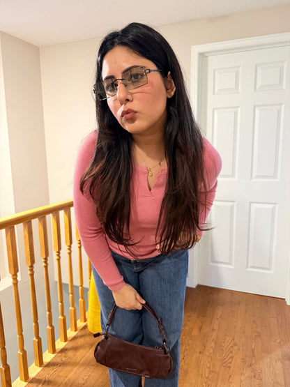 Woman in pink shirt and blue jeans holding a brown bag in a room with wooden floor and white door.