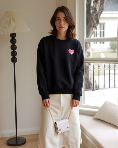 Woman wearing a white sweatshirt with a pink heart design on a plain background
