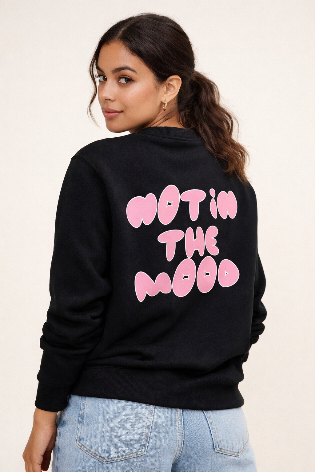 Woman wearing a black sweatshirt with pink text on the back against a beige background