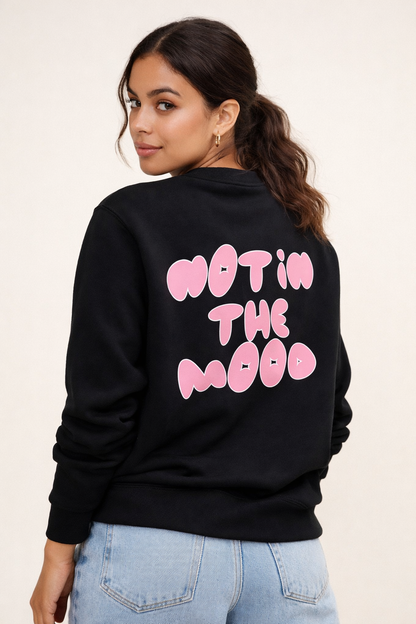 Woman wearing a black sweatshirt with pink text on the back against a beige background