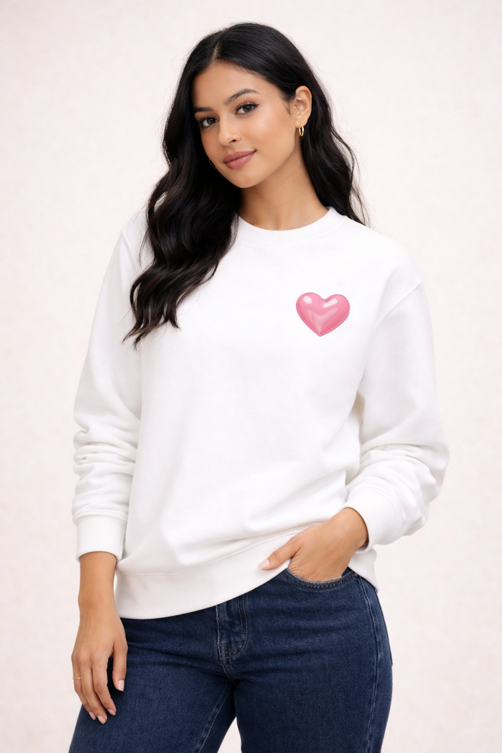 Woman wearing a white sweatshirt with a pink heart design on a plain background